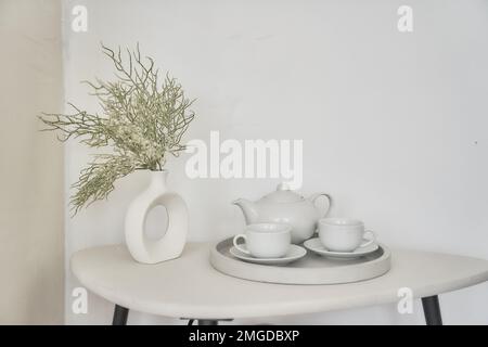 Una composizione minimalistica per una colazione festosa con piatti bianchi, un bouquet di fiori secchi in vaso su sfondo chiaro. Con un luogo per copiare. Foto di alta qualità Foto Stock