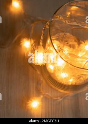 Vista dall'alto del vaso di vetro con ghirlanda luminosa dorata di Natale da lampadine a LED con soffice palla o punta in vaso di vetro su sfondo tavolo di legno. Top vie Foto Stock