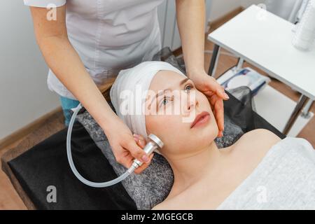 Giovane donna sorridente cosmetologa con rullo facendo massaggio natiche Foto Stock