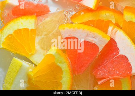 Pezzi di pompelmo, arancia e miele pomelo in liquido con bolle. Fettine di pompelmo, arancia e melelo di miele in acqua. Fetta fresca Foto Stock