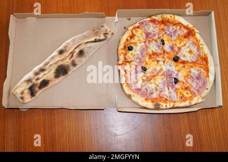 Pizza classica appena sfornata e rotolo calzone scatola di cartone su tavolo di legno in vista dall'alto Foto Stock