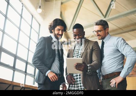Il nostro sito Web è fantastico per i dispositivi mobili. tre uomini d'affari ben vestiti che si riuniscono in un tablet in ufficio. Foto Stock
