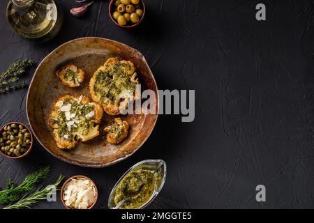 Bistecca di cavolfiore con spezie, salsa di chimichurri, fiocchi di mandorle. Capperi, olive, erbe, fianco a fianco. Sfondo scuro. Cibo vegetariano. CopySpace. Foto Stock