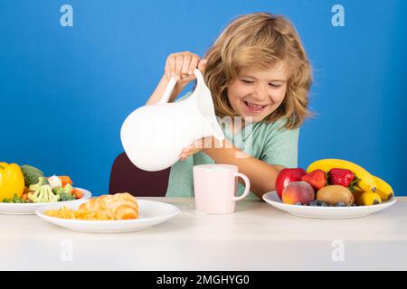 Capretto che versa latte intero di mucche. Ritratto di bambino mangiare cibo fresco sano in cucina a casa. Bambino che mangia la colazione prima della scuola. Bevanda per bambini Foto Stock