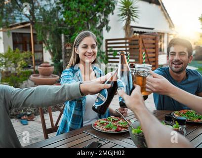 Lasciate che i tempi buoni rotolino. un gruppo di giovani amici che sorregge un drink e brinda all'esterno intorno ad un tavolo per celebrare la loro amicizia. Foto Stock