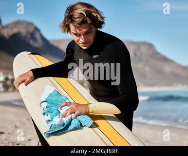 Surf, uomo con tavola da surf in spiaggia con fitness e viaggi, pulizia tavola e manutenzione surf con sport estremi all'aperto. Oceano. natura e. Foto Stock