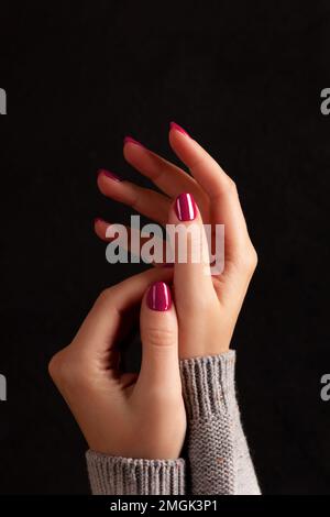 Maniche femminili in maglia grigia con bella manicure - viva magenta, unghie rosa su fondo nero scuro. Concetto di cura delle unghie Foto Stock