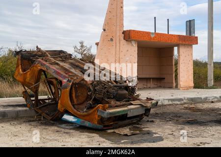 Campagna. Un'auto civile bruciata rovesciata si trova in una stazione degli autobus. Guerra in Ucraina. Invasione russa dell'Ucraina. Crimini di guerra Foto Stock