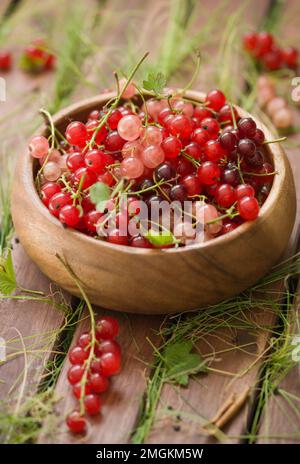 Bacche colorate fresche di un ribes in una ciotola di legno su un tavolo di legno. Foto Stock