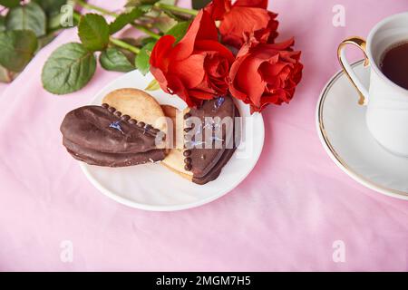 Cibo di San Valentino, biscotti vegani e tazza di caffè. Rose rosse estetica, romantico sfondo di vacanza rosa lagom. Foto Stock