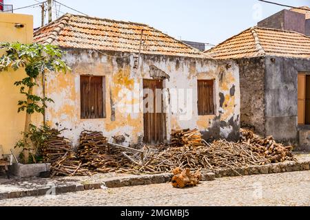 Un cottage in pietra fatiscente con tronchi e legna da ardere di fronte alla porta d'ingresso e sul marciapiede, Fogo Island, Capo Verde Foto Stock