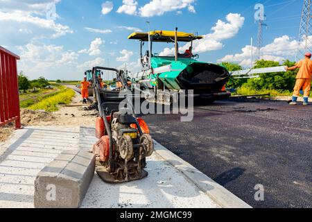 Macchina a piastre vibranti per la compattazione di asfalto parcheggiato sul ponte incompiuto. La macchina spalmatrice depone, versa l'asfalto caldo Foto Stock