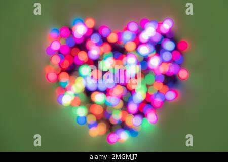 Luci arcobaleno fortemente sfocate ripiegate a forma di cuore su sfondo verde per San Valentino Foto Stock
