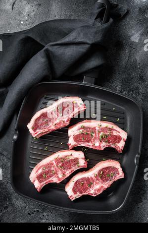 Costolette di costolette di agnello crudo in padella grigliata con rosmarino e timo. Sfondo nero. Vista dall'alto Foto Stock