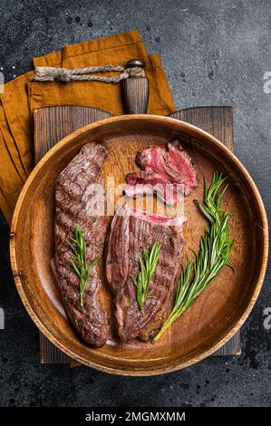 Lembo di controfiletto fritto o bistecca di manzo con erbe aromatiche in un piatto di legno. Sfondo nero. Vista dall'alto Foto Stock