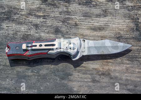 Coltello pieghevole sullo sfondo di una vecchia struttura in legno. Foto Stock