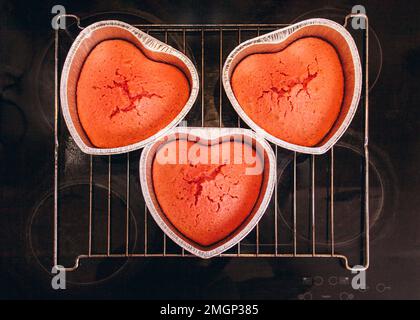 Tre torte rosse in una teglia a forma di cuore sono sul piano cottura a casa. Preparazione per San Valentino Foto Stock