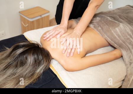 massaggiatore donna che massaggia la schiena di una giovane donna su un tavolo da massaggio nella sala spa Foto Stock