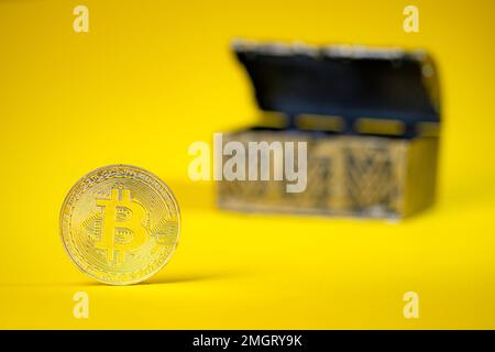 Bitcoin su sfondo giallo. Casella del tesoro sfocata sullo sfondo. Investire denaro nel mercato cripto. Foto Stock