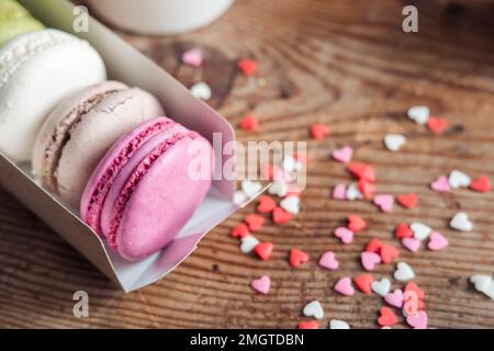 Macaron assortiti in una scatola cosparsa di piccoli cuori su uno sfondo di legno, vista dall'alto Foto Stock