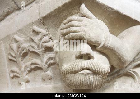 Testa grottesca in pietra scolpita di un uomo apparentemente affetto da mal di testa, su una colonna del 12th ° secolo nella Chiesa di San Giovanni Battista, Bere Regis, Dorset. Foto Stock