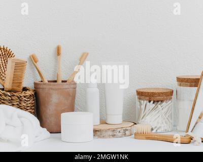 Vista frontale dello sfondo del bagno con scatola di paglia, accessori personali, cosmetici, vasetti e asciugamani bianchi su sfondo bianco. Vista frontale. Spazio di copia Foto Stock