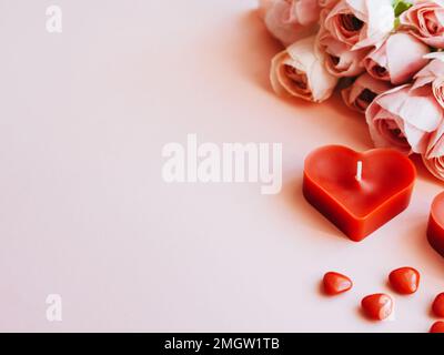 Rosa ranuncolo fiorito su sfondo rosa festivo, pastello bouquet carta floreale, candele rosse e cuori dolci confetti. Buon giorno di San Valentino Foto Stock