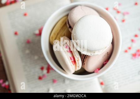 Macaroon in una ciotola su uno sfondo libro di piccoli cuori su uno sfondo di legno, vista dall'alto Foto Stock