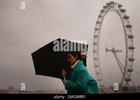 Una donna si copre contro il tempo umido e ventoso sul Westminster Bridge nel centro di Londra. Data immagine: Giovedì 26 gennaio 2023. Foto Stock