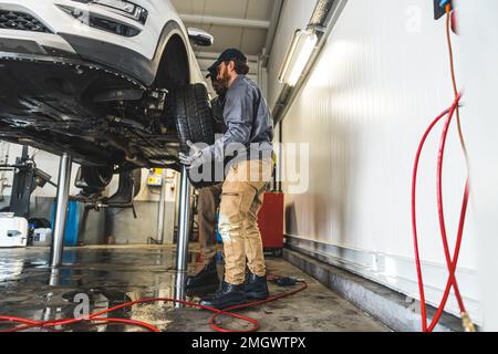 I meccanici dell'automobile sono occupati sostituire le ruote di un'automobile sull'ascensore in un negozio di riparazione auto. Foto di alta qualità Foto Stock