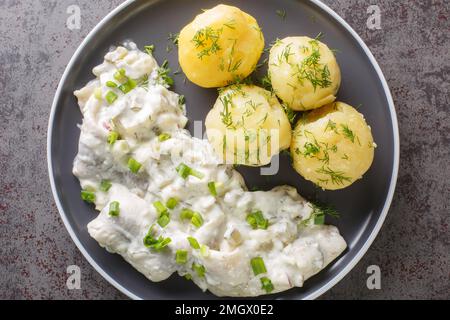 Filetto di aringa piccante in salsa cremosa con contorno di patate bollite in un piatto sul tavolo. vista orizzontale dall'alto Foto Stock