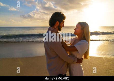 Coppia appena impegnata godendo di un romantico abbraccio durante l'ora d'oro su una spiaggia di sabbia vuota Foto Stock
