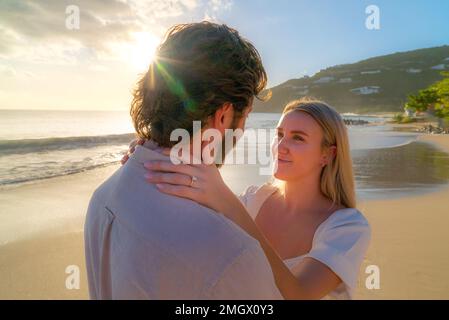 Coppia appena impegnata godendo di un romantico abbraccio durante l'ora d'oro su una spiaggia di sabbia vuota Foto Stock