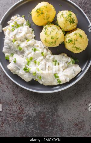 Cibo tedesco Filetto di aringa Sahnehering in salsa cremosa con patate bollite guarnire in un piatto sul tavolo. vista verticale dall'alto Foto Stock