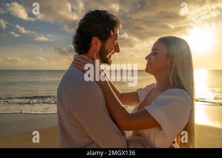 Coppia appena impegnata godendo di un romantico abbraccio durante l'ora d'oro su una spiaggia di sabbia vuota Foto Stock