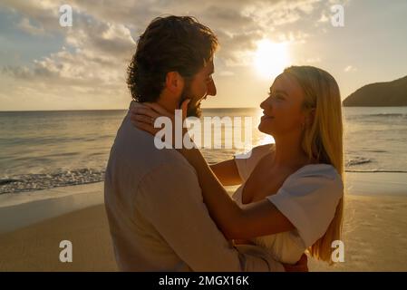 Coppia appena impegnata godendo di un romantico abbraccio durante l'ora d'oro su una spiaggia di sabbia vuota Foto Stock