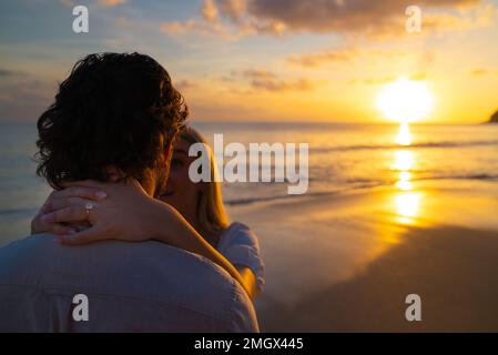 Giovane coppia appena impegnata su una spiaggia tropicale vuota durante il tramonto sull'oceano Foto Stock