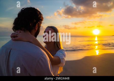 Giovane coppia appena impegnata su una spiaggia tropicale vuota durante il tramonto sull'oceano Foto Stock