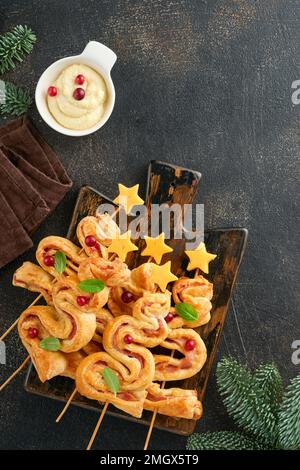 Antipasto di Natale o Capodanno. Panini di pasta sfoglia a forma di albero di Natale con formaggio e prosciutto. Gruppo di forme di albero di Natale su tavola di legno. documento d'identità festivo Foto Stock