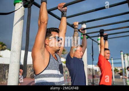 Tre uomini allenano facendo pull up in una palestra all'aperto, sport e stile di vita sano Foto Stock