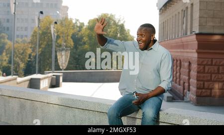 Anziano uomo di mezza età in città in attesa della data di incontro agitando la mano venire qui gesto di benvenuto. Pensione uomo d'affari afro-americano maschio Foto Stock
