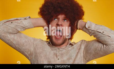 Non vuoi ascoltare e ascoltare. Frustrato irritato uomo afro acconciatura irritata coprendo le orecchie e gesturando no, evitando consiglio ignorando sgradevole rumore voci forte. Ragazzo Hippster su sfondo giallo Foto Stock