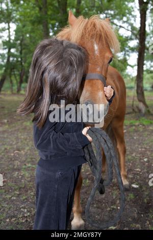 Una bambina che bacia e il suo pony rosso shetland Foto Stock