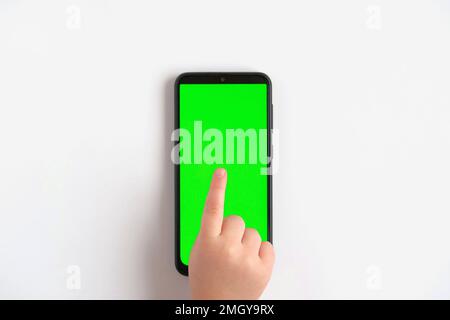 Mano del bambino che tocca scattandosi sul telefono mobile con lo schermo chromakey. Little Baby tocca il dito al centro del display verde vuoto del telefono. Primo piano 4K Fo Foto Stock