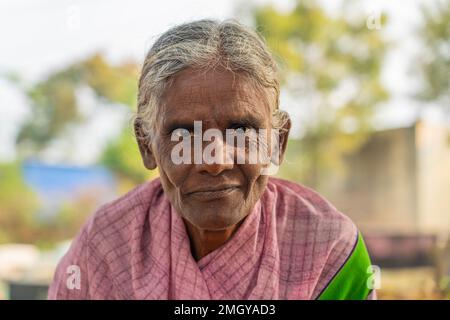 Puttaarthi, India - Gennaio 21,2023: Vecchia signora indiana primo piano guardando in macchina fotografica ad un mercato di verdure a Puttaarthi Foto Stock