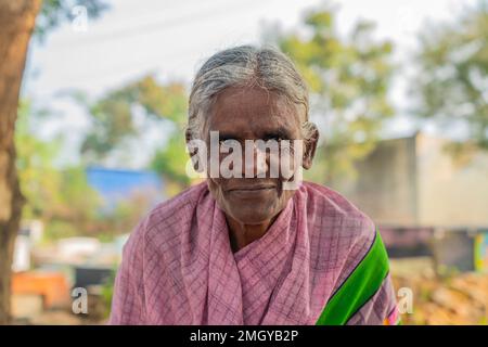 Puttaarthi, India - Gennaio 21,2023: Vecchia signora indiana primo piano guardando in macchina fotografica ad un mercato di verdure a Puttaarthi Foto Stock