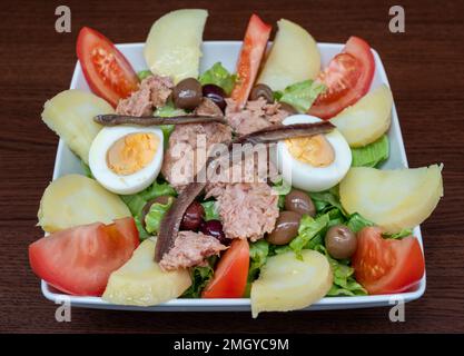 Insalata di Nicois in un piatto quadrato su uno sfondo di legno. Foto Stock