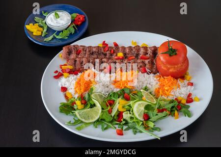 Lula kebab di pollo di vitello con riso, verdure e salsa su sfondo nero. Foto Stock