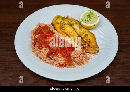 Filetto di pesce fritto fresco guarnito con riso in salsa di pomodoro ed erbe aromatiche. Foto Stock