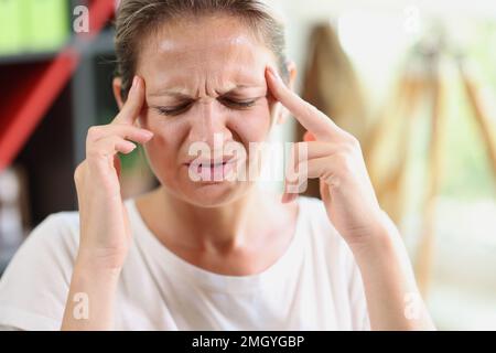 Donna triste e stanca con le mani che toccano la fronte che soffre di mal di testa, emicrania o depressione Foto Stock